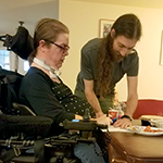 Woman in a wheelchair and a man at a table.