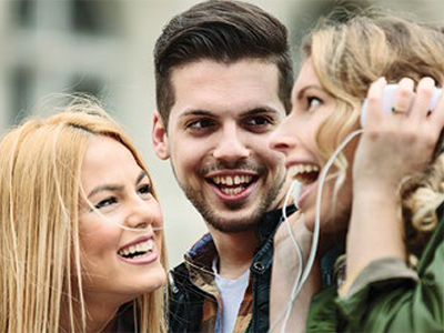 3 teenagers, with one listening to music while other two watch her laugh.